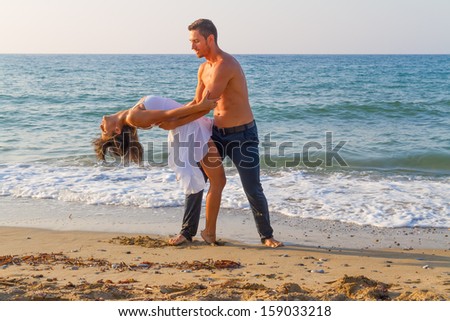 Summer afternoon at a sandy beach with the ocean in the background, a young couple practices a dance scene. 