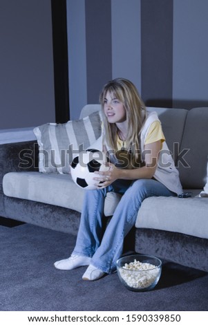 Young woman watching television with soccer ball