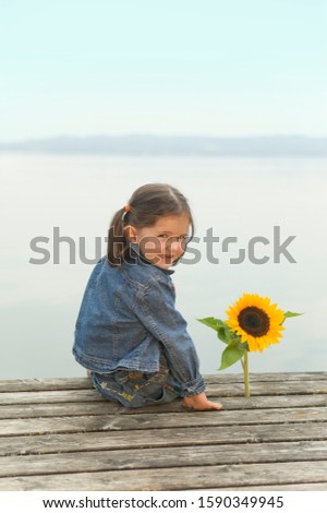 Young girl sitting on pier at lake with sunflower