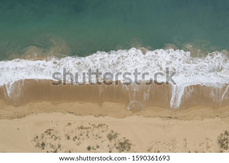 An aerial shot of the beautiful foamy ocean waves meeting the sands on the beach
