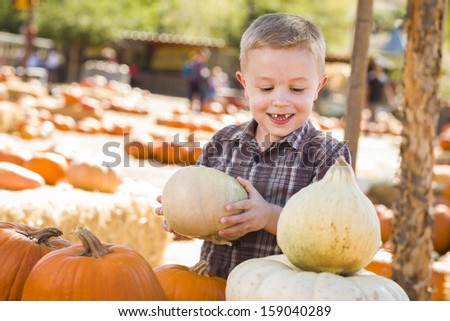 Adorable Little Boy Gathering His Pumpkins at a Pumpkin Patch on a Fall Day. 