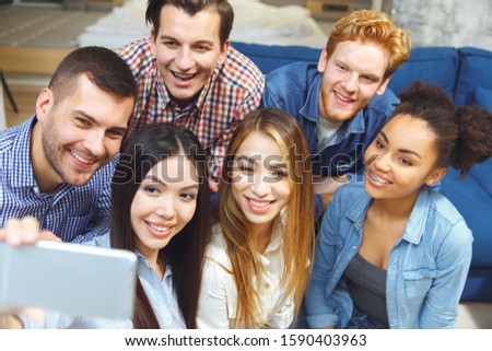 Young men and women having fun taking selfie pictures for social media together indoors top view close-up smiling happy