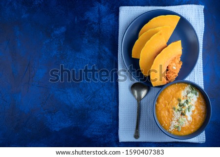 pumpkin cream soup in a blue plate on a deep classic blue background with slices of pumpkin with blue textile and a spoon. flat lay. copy space.
