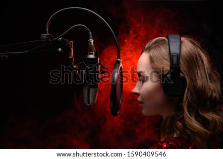 Vocalist, celebrity sings in a studio microphone with headphones on her head, live performance, vocals, vocal studio, recording a track. Against a background of red smoke