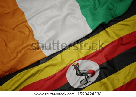 waving colorful flag of uganda and national flag of cote divoire. macro