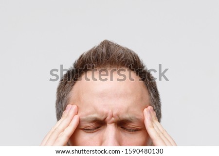 Headache, nervous tension, temporal and throbbing pain concept. Close up portrait of man massaging his temples, closed eye, isolated on gray background. Strong migraine
