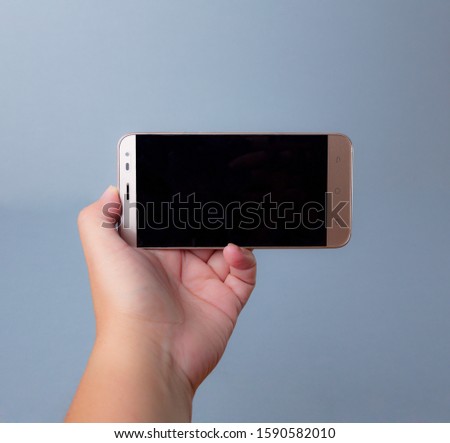 Phone in hand on bluish background and with black screen.