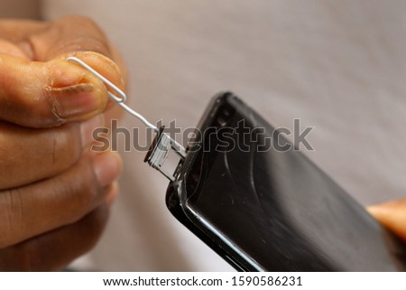 Alternatively, without eject tool, male hand holding mobile phone using paperclip inserting into mobile phone eject hole to eject sim card  Royalty-Free Stock Photo #1590586231