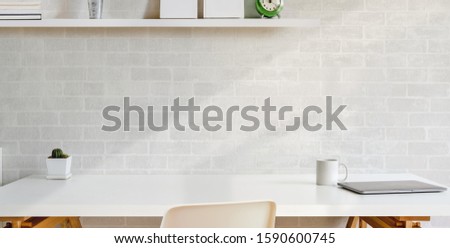 Cropped shot of comfortable workplace with office sullies on wooden table and white brick wall background 