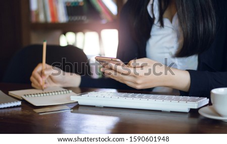 Close-up of hand young businesswoman using mobile phone working with computer and writing information on notebook 