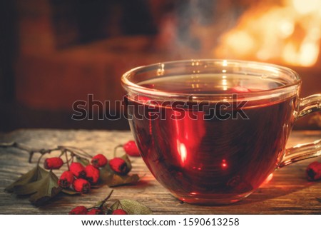Tea with hawthorn in a glass cup on a wooden table in a room with a burning fireplace