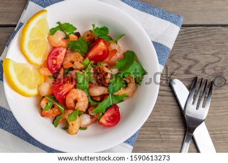Fresh homemade salad of shrimp, arugula and tomato in a white plate on a wooden table, top view, flat lay, close up