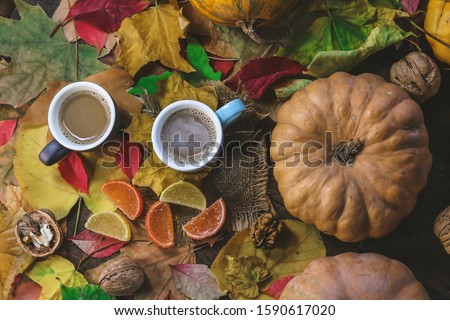 cup of coffee with milk on a wooden kitchen table on a background of autumn leaves and pumpkins.