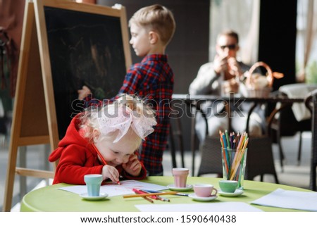 Children draw. Blonde girl sits at a table, a boy stands near a blackboard.