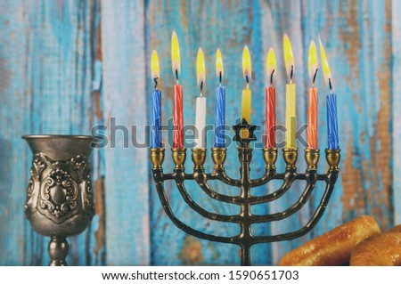 Menorah with colored burning candels and silver cup of wine.