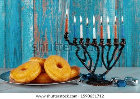 Jewish holiday Hanukkah background with menorah, burning candles and donuts on plate.