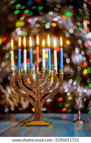 Hanukkah background with menorah and burning candles on sparkle background with defocused colored lights.