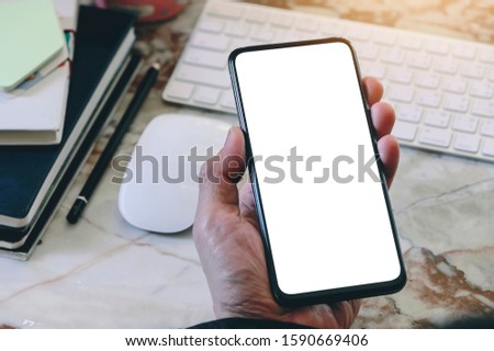 Cropped shot of man hand holding smartphone with blank screen while sitting at office desk, blank screen for text or graphic design.