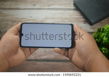 Close up man hand holding smartphone between a vase and coffee on wooden table