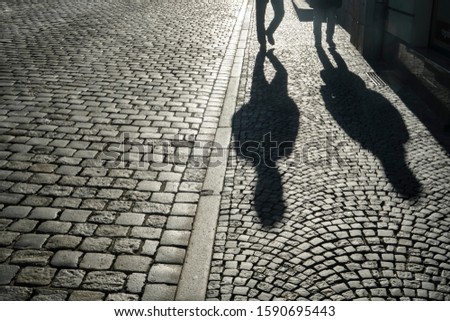 Clear shadows of people on a cobblestone pavement. european  pedestrian street in sunset light in summer evening. Black and white. homosexual couple of gays. 
