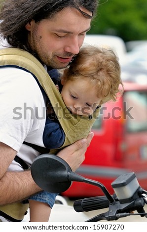 father and his baby-boy in sling carrier look at motorbike