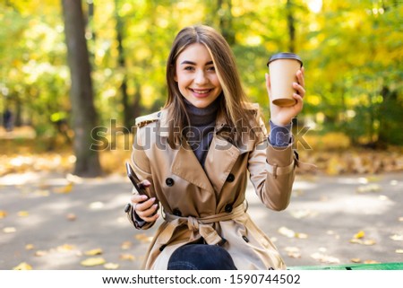 Beautiful woman sitting with coffee in autumn city park, fall season, yellow leaves