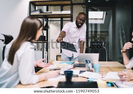 Dissatisfied modern African American leader presenting data on paper to colleagues and frowning while explaining problems with report meeting in office
