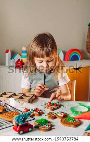 Little girl decorating Christmas gingerbread cookies with sprinkles and chocolate candies. 