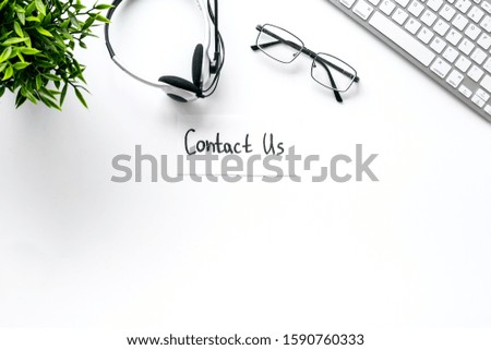 Customer support service concept. Text Contact Us near headset on white office desk top-down copy space