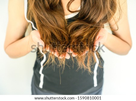 Cropped shot view of woman holding her damaged split ended hair (Focus at ends hair). Hair damage is risk for further damage and breakage. It may also look dull or frizzy and be difficult to manage. Royalty-Free Stock Photo #1590810001