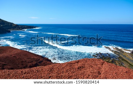 Red volcanic rocks on the slopes of the lake with green water. Canary Islands. Lanzarote, volcanic island. The magnificent coast of the Atlantic Ocean.
