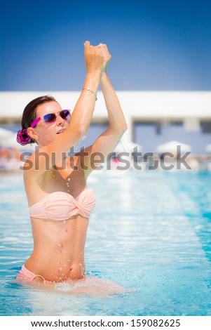Pretty woman playing with water drops in the pool. 