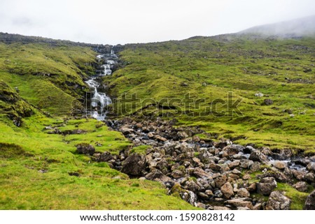 Peaceful waterfall flows downhill from mountain covered with fog, nordic landscape photo.