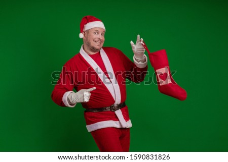 Emotional Santa Claus holds a Christmas sock for gifts in his hands and poses on a green chrome background