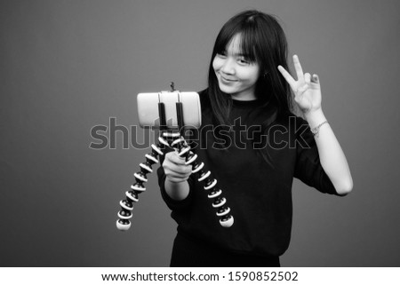 Young beautiful Asian woman wearing black sweater against gray background