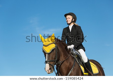 Teenage girl riding a horse on a background of blue sky.