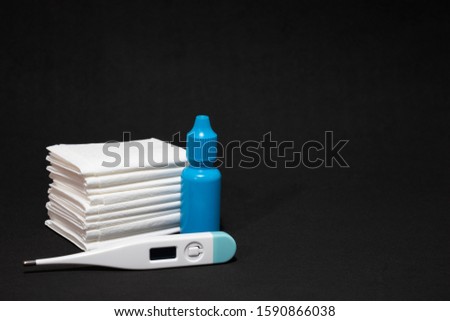 White paper tissues and white thermometer with blue nose drops on dark back background.