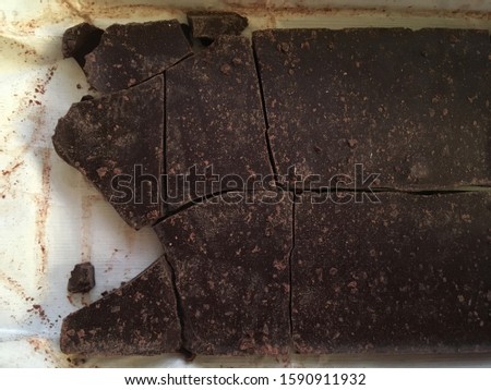 Closeup of cracked bar of dark chocolate lying on a piece of paper