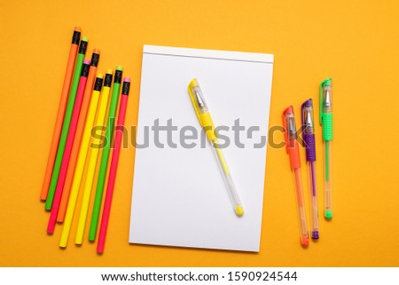 white sheet of notebook, colored pens and pencils on yellow background