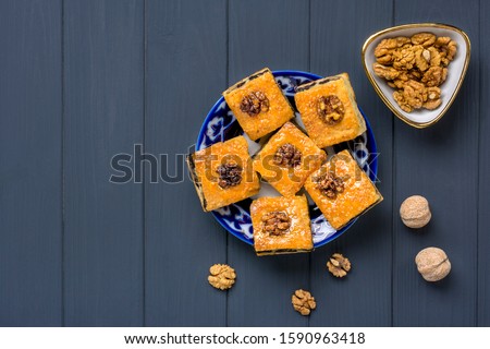 Traditional arabic dessert baklava with cashew, walnuts, raisins on plate with Uzbek national ornament on dark grey wooden table. Homemade baklava with nuts and honey Top view Flat Lay