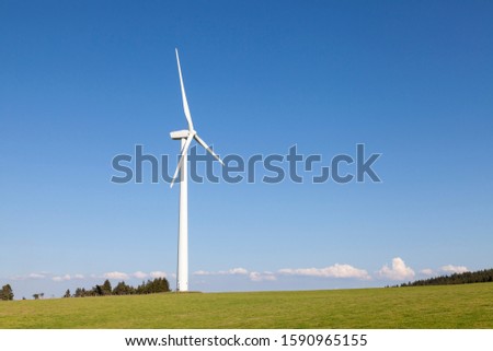 Single wind turbine in a lush  hilltop pasture providing green renewable electricity from conversion of natural kinetic energy of the wind. Industry and agriculture  Royalty-Free Stock Photo #1590965155
