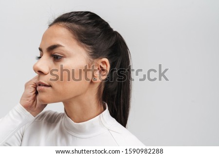 Image of young brunette woman in sportswear putting on earpods isolated over gray background
