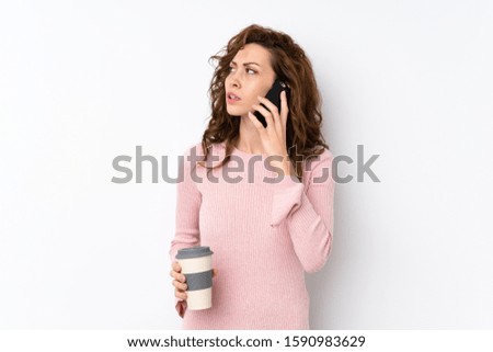 Young pretty woman over isolated background holding coffee to take away and a mobile