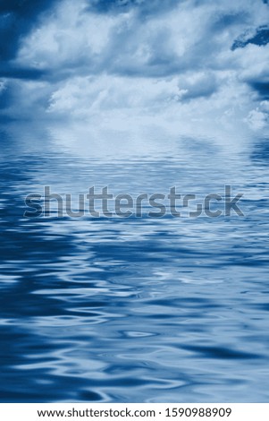 Blue clear sea water background with waves and reflections of the sky and fluffy clouds. Color of the year 2020 classic blue toned