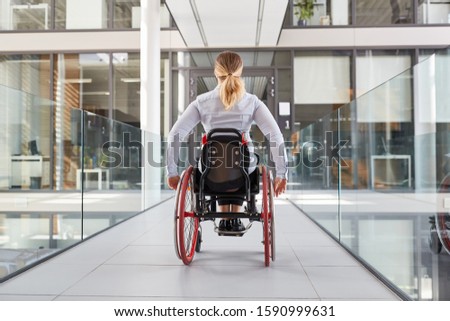 Paralyzed woman in a wheelchair on the move in the disabled office building Royalty-Free Stock Photo #1590999631