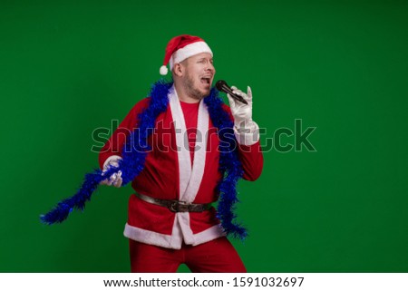 Emotional Santa Claus and a blue garland of tinsel holds a microphone in his hands, sings and gestures on a green chrome background