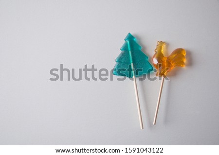 Green and yellow Christmas candy canes with wooden sticks. Christmas tree and cock on a white background. Holiday picture. New year wallpapers. Post card. Composition of sweets. Two conifers.
