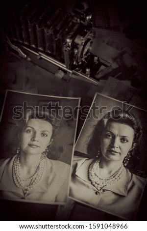 Old prints of portraits lie on the table against the background of a vintage large format film camera. Design element.