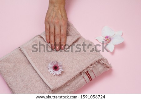 Soft terry towel and woman's hand with flowers on pink background. Top view.