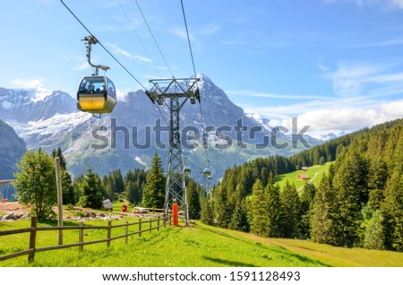 Yellow cable car in the Swiss Alps. Gondola going from Grindelwald to First in the Jungfrau area. Summer Alpine landscape with snowcapped mountains in the background. Transport tourists uphill. Royalty-Free Stock Photo #1591128493
